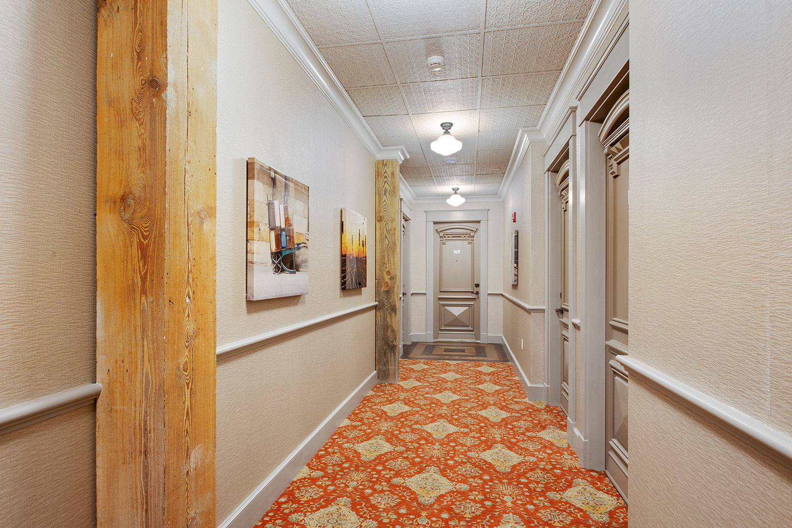 a long hallway with white walls, orange carpet, and paintings on the wall