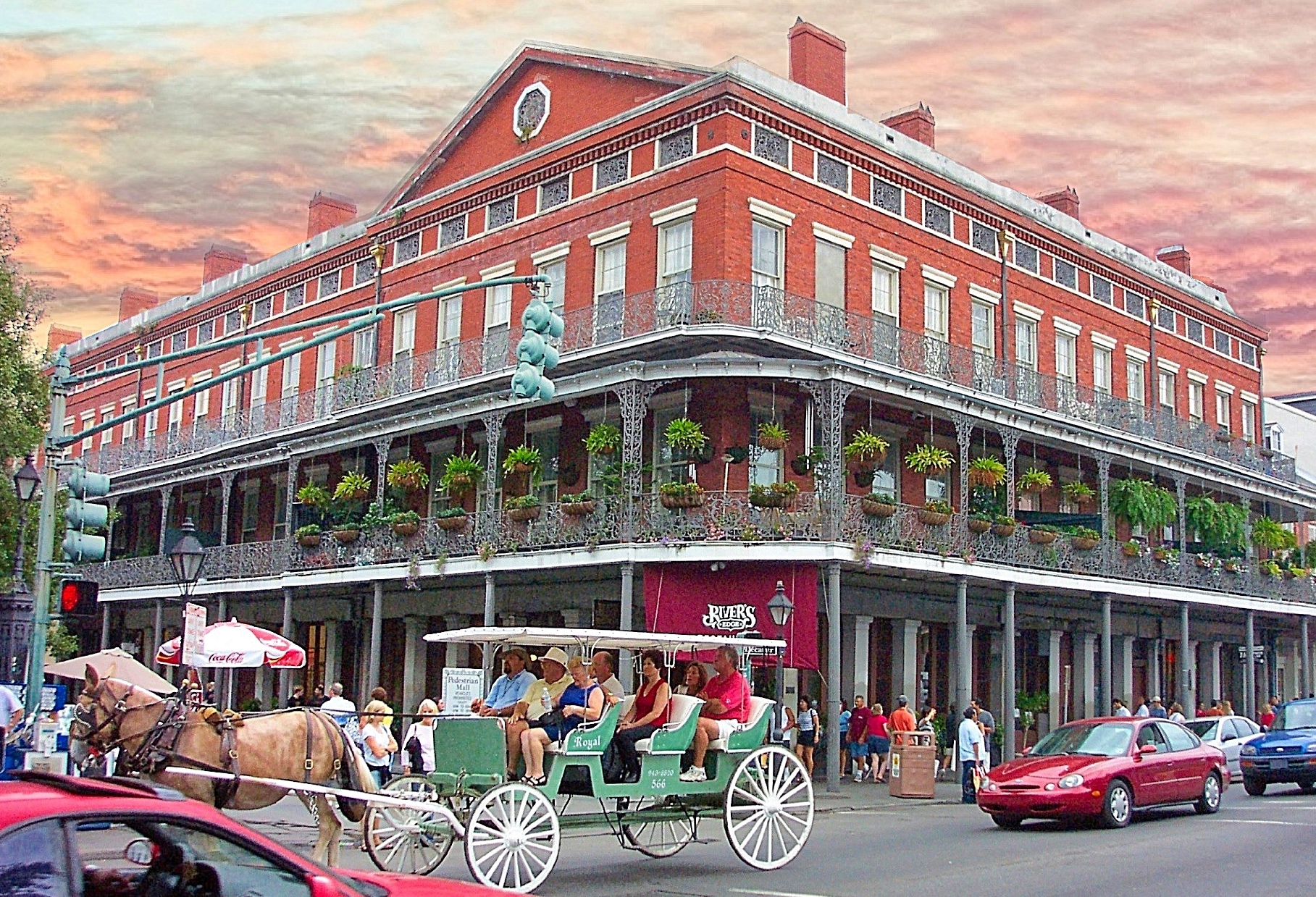 A red brick building with balconies and columns on a street with a horse-drawn carriage and cars.